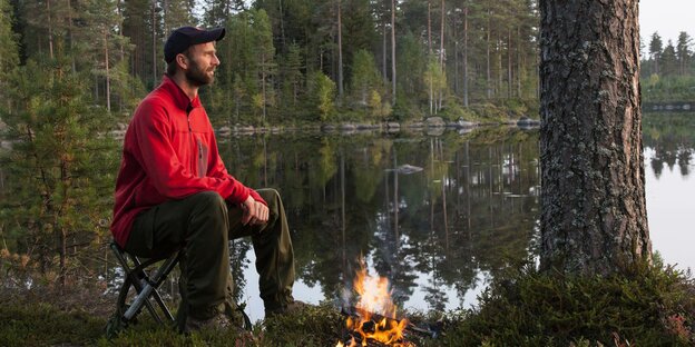 Ein Mann mit Lagerfeuer im Wald am See.