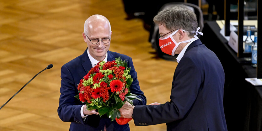 Ein Mann mit Mund-Nase-Schutzmaske überreicht einem anderen Mann Blumen