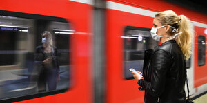 Eine Frau mit Mundschutz steht auf einem Bahnsteig neben einem einfahrenden Zug.