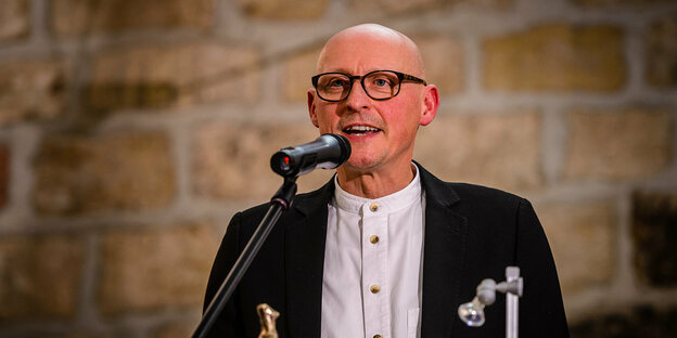 Jörg Bernig, ein älterer glatzköpfiger Mann,spricht am Mikrophon