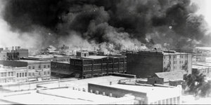 Ein Schwarz-weiß-Foto - Ansicht einer Stadt von erhöhter Perspektive. Dichter schwarzer Rauch steigt über den Dächern auf