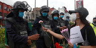 Eine Frau mit Mundschutz verteilt während einer Demonstration Blumen an Polizisten.