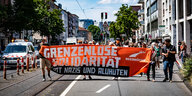 Protestierende der Seebrücke mit Mundschutz halten ein oranges Transparent mit der Aufschrift "Grenzenlose Solidarität statt Nazis und Aluhüten"