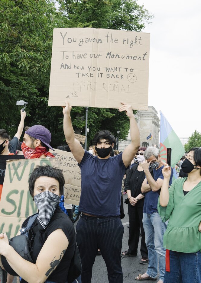 Ein Mann hält ein Plakat in den Händen und fordert den Erhalt des Mahnmals für die ermordeten Sinti und Roma