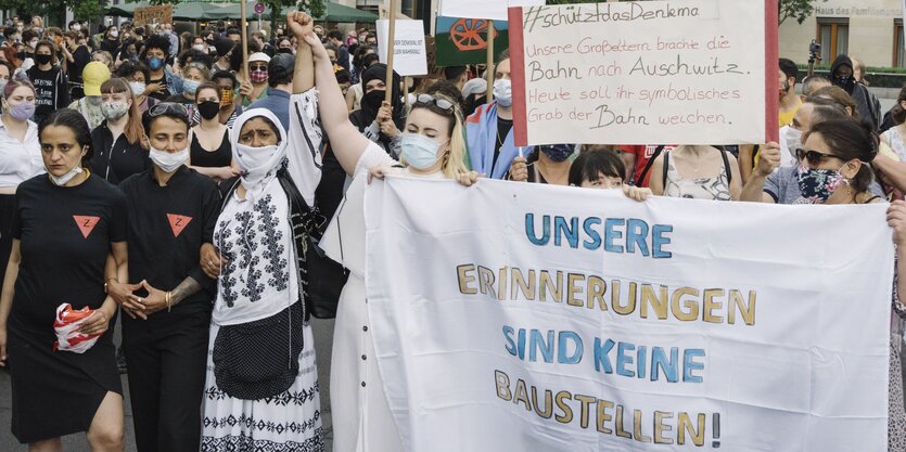 Viele Frauen und Männer bei eine Demo mit Plakaten und Spruchbändern zum Erhalt des Mahnmals für die ermordeten Sinti und Roma