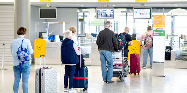 Menschen stehen mit Gepäck und Sicherheitsabstand am Check-In-Schalter Menschen stehen mit Gepäck und Sicherheitsabstand am Check-In-Schalter