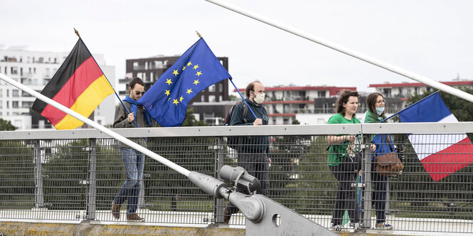 Demonstrierende laufen über eine Brücke und tragen Masken.