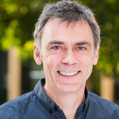 Ein Portraitfoto zeigt Frank Kalter, Co-Direktor des DeZIM. Er lächelt und trägt ein dunkelblaues Hemd, im Hintergrund sind Bäume zu sehen.