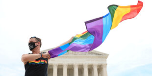 Ein Mann mit einer Maske schwingt die Regenbogenfahne vor dem Gebäude des Obersten Gerichgtshofes der USA