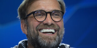 Jürgen Klopp lachend vor einem blauen Hintergrund.