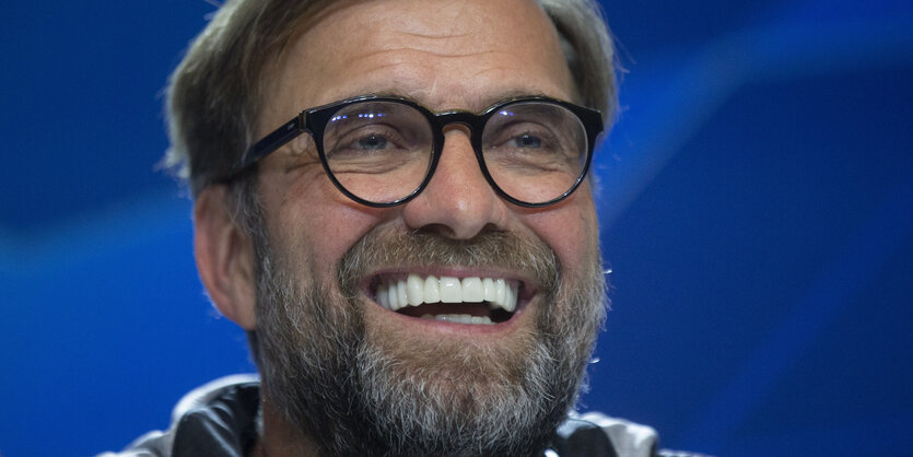 Jürgen Klopp lachend vor einem blauen Hintergrund.