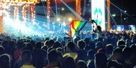 Auf einem Rockkonzert hält ein Mensch eine Regenbogenfahne über die Menge