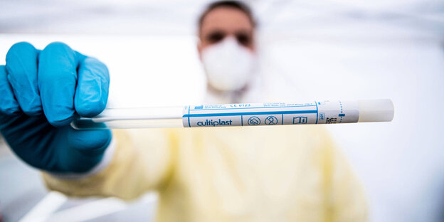 Person mit Mundschutz hält einen Coronatest in einem Testzentrum in die Kamera