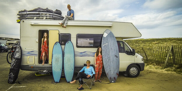 Eine Familie mit Van hat sich mit ihren Surfbrettern vor ein Wohnmobil gestellt