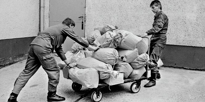 Zwei Personen mit einem Handwagen mit Säcken darauf.