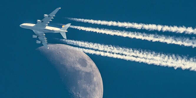 Ein Flugzeug mit langen Kondensstreifen scheint den Mond zu berühren