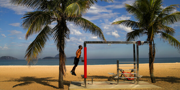 Unter Palmen am Strand trainiert ein muskulöser Mann