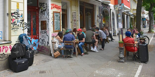Strasse mit Tischen und Gästen eines Lokals, daneben Koffer auf dem Bürgersteig