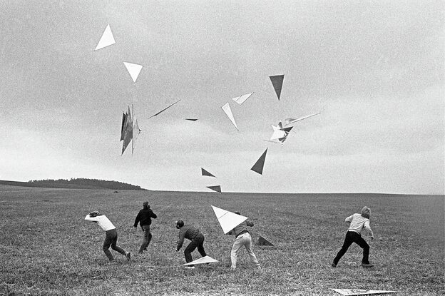 Vier Männer und eine Frau werfen Dreiecke in die Luft, die wie Drachen steigen