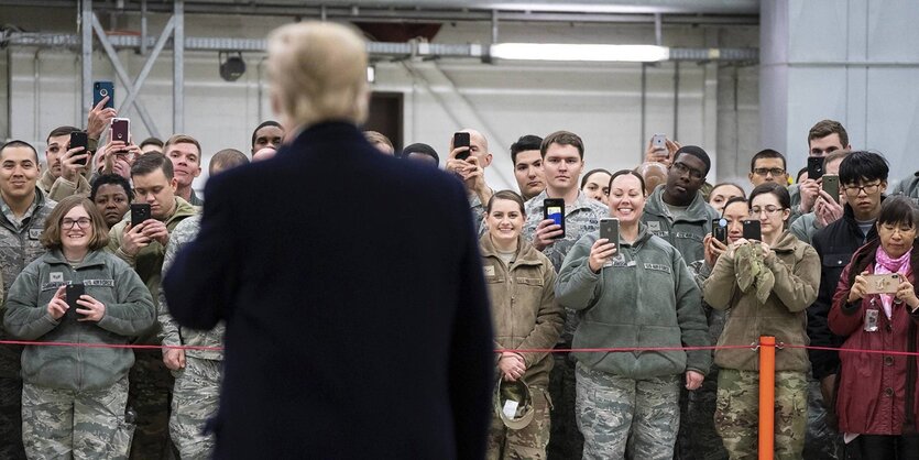 Ein Mann von hinten vor vielen SoldatInnen mit Smartphones.