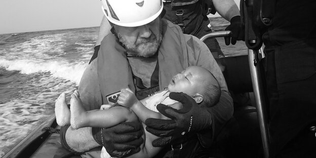 Ein Mann auf einem Boot hält ein totes Baby in seinen Armen
