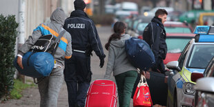 Polizisten stehen mit mehreren Menschen mit Koffern auf dem Bürgersteig