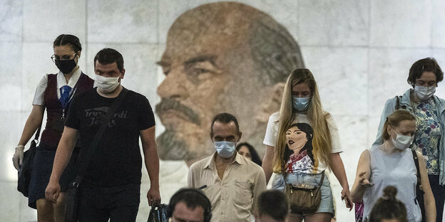 Vor einem Lenin Mosaik steigen Menschen in eine U-Bahn mit Schutzmasken