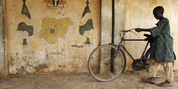 Junge schiebt sein Fahrrad, daneben auf eine Wand gemalt die Karte Nigerias