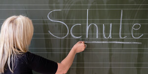 Eine Grundschullehrerin schreibt das Wort "Schule" auf eine Schultafel in einem Klassenzimmer.