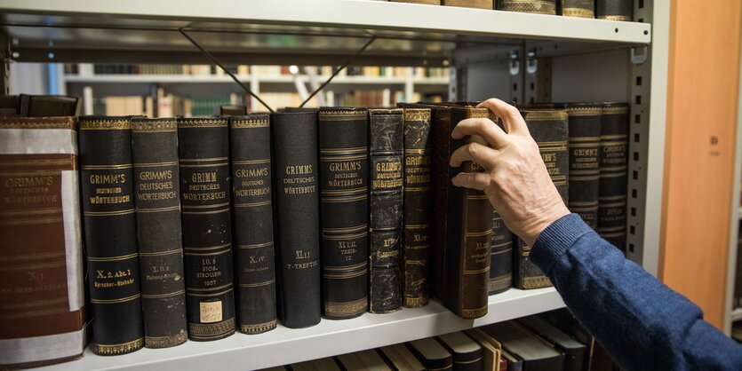 Eine Hand greift nach alten Büchern in einem Regal