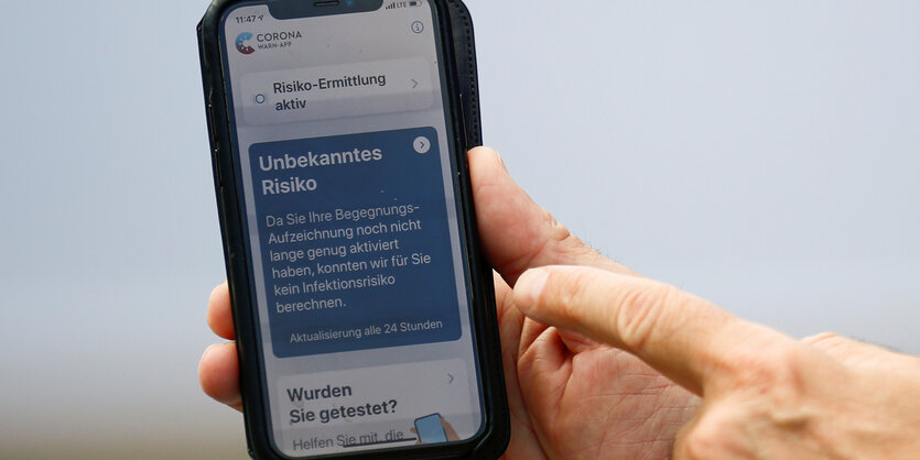 Eine Hand zeigt auf ein Handy, auf das die Corona-App geladen ist