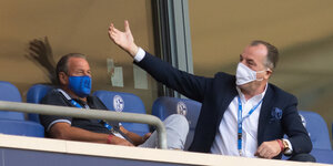 Clemens Tönnies auf einem Stadiontribünensitz, er beugt sich nach vorne ans Geländer und macht mit seinem rechten Arm eine ausladende Bewegung. Er trägt Maske, wie sein Sitznachbar