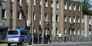 PolizistInnen vor einem Wohnblock, dazwischen ein Zaun