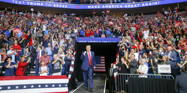 Donald Trump betritt eine Arena. Auf den Rängen sitzen viele Menschen.