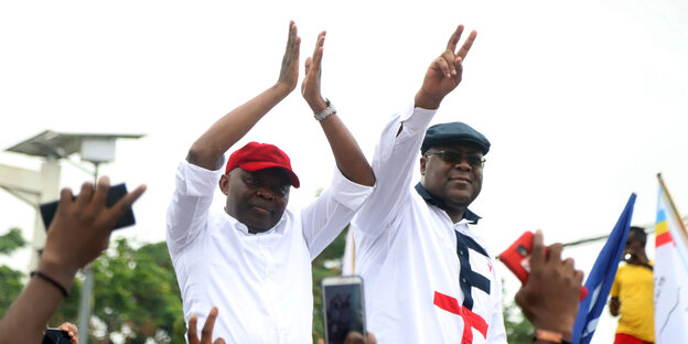 Kamerhe steht links, neben im Präsident Tshisekedi. Beide tragen weiße Hemden und heben die Arme in die Luft.