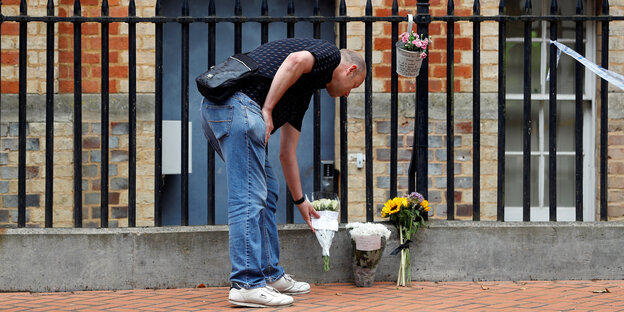 ein Mann legt Blumen an einem Gitterzaun nieder