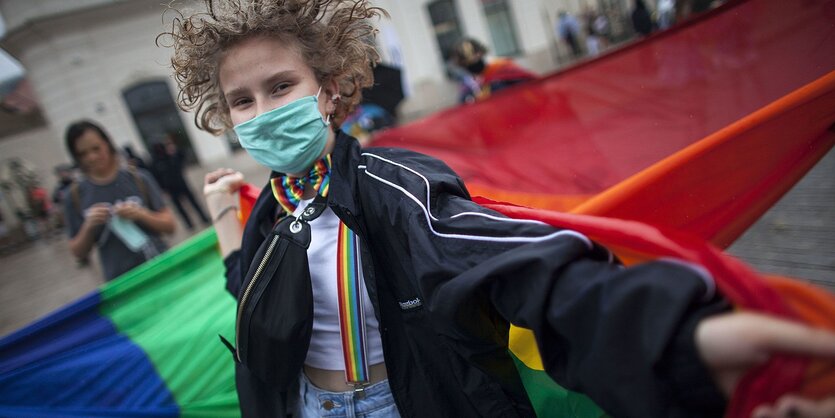 Eine Person tanzt vor einer Regenbogenfahne