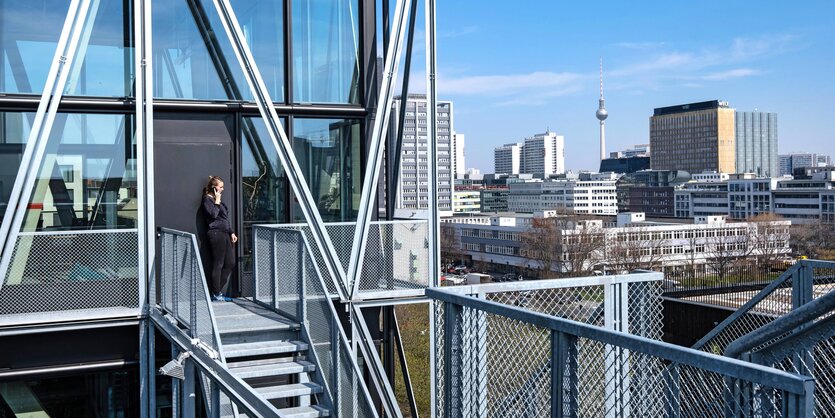 Eine Frau telefoniert auf einer Treppe des taz Gebäudes im Hintergrund das Gebäude der Welt