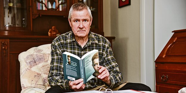 Günter Wulf sitzt in einem Sessel und hält sein Buch in den Händen.