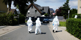 Drei Personen in Schutzanzügen laufen durch ein Gütersloher Wohngebiet.