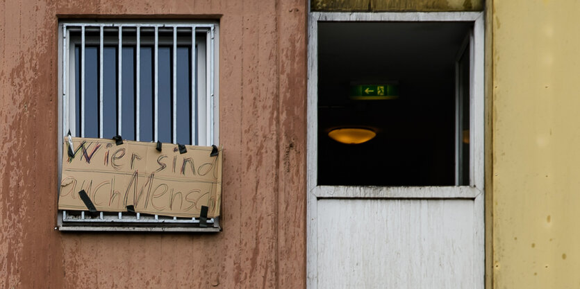 Wir sind auch Menschen steht auf einem SChild im vergitterten Fenster