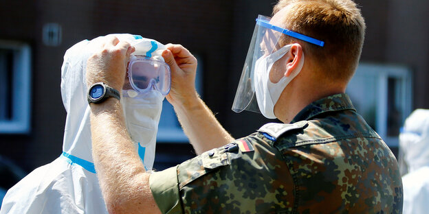 Ein Mitglied der Bundeswehr richtet einem Gesundheitsmitarbeiter die Schutzbrille.