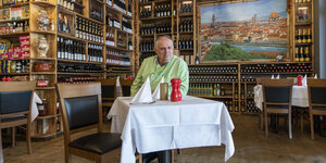 Regale mit Wein und ein Tisch mit weißer Tischdecke, an dem sitzt Mario Dzeladini, Inhaber des italienischen Restaurants „Firenze“ in Pankow