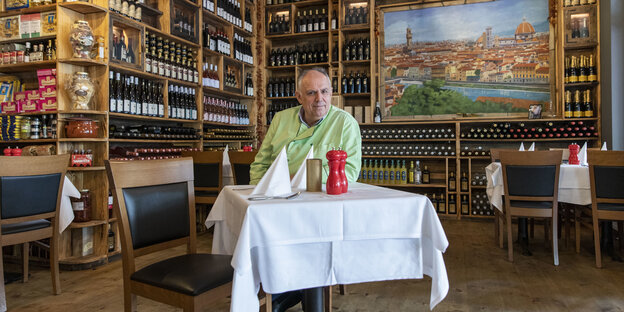 Regale mit Wein und ein Tisch mit weißer Tischdecke, an dem sitzt Mario Dzeladini, Inhaber des italienischen Restaurants „Firenze“ in Pankow