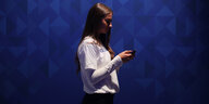 Frau im weißen Shirt vor blauem Hintergrund schaut in ihr Handy