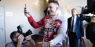 Rapper Gzuz mit Goldkette und Rolex filmt lachend einen Fotografen im Gericht