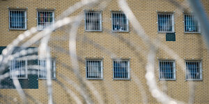 Die Fenster der Justizvollzugsanstalt (JVA) Hannover vor dem Einbau der Lochbleche: Einfache Gitter vor den Zellen reichen, im Vordergrund ist ein Maschendrahtzaun zu sehen, der das Gefängnis umschließt