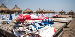 Sonnenschirme liegen am Strand von Lara auf leeren Strandliegen.