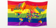 Ein Wandtuch mit den PACE-Regenbogenfarben. Darauf die Kontinente, ebenfalls in den Farben gehalten