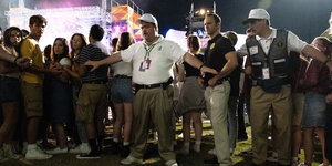Ein korpulenter Mann im weißen Hemd spannt die Arme aus, um andere Menschen zurück zuhalten.